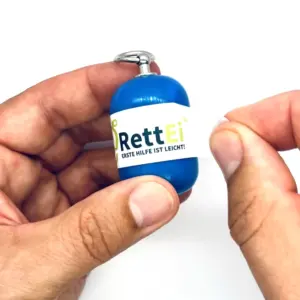 Notfall-Set-fuer-unterwegs-als-RettEi-Original-via-Erste-Hilfe-Schluesselanhaenger-mit-Beatmungstuch-zur-Mund-zu-Mund-Beatmung-mit-blauer-Kapsel-beim-oeffnen.