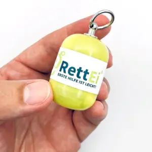Notfall-Set-fuer-unterwegs-als-RettEi-Original-via-Erste-Hilfe-Schluesselanhaenger-mit-Beatmungstuch-zur-Mund-zu-Mund-Beatmung-mit-gelb-Kapsel-in-Hand.