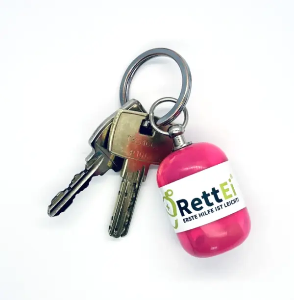 Notfall-Set-fuer-unterwegs-als-RettEi-Original-via-Erste-Hilfe-Schluesselanhaenger-mit-Beatmungstuch-zur-Mund-zu-Mund-Beatmung-mit-rosa-Kapsel-am-Schluesselbund.