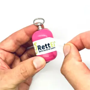 Notfall-Set-fuer-unterwegs-als-RettEi-Original-via-Erste-Hilfe-Schluesselanhaenger-mit-Beatmungstuch-zur-Mund-zu-Mund-Beatmung-mit-rosa-Kapsel-beim-oeffnen.
