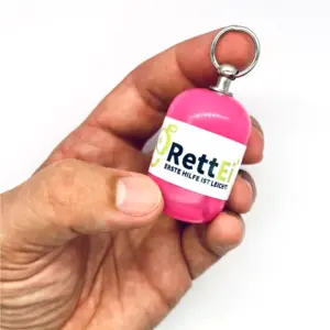 Notfall-Set-fuer-unterwegs-als-RettEi-Original-via-Erste-Hilfe-Schluesselanhaenger-mit-Beatmungstuch-zur-Mund-zu-Mund-Beatmung-mit-rosa-Kapsel-in-Hand.