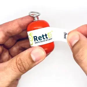 Notfall-Set-fuer-unterwegs-als-RettEi-Original-via-Erste-Hilfe-Schluesselanhaenger-mit-Beatmungstuch-zur-Mund-zu-Mund-Beatmung-mit-roter-Kapsel-beim-oeffnen