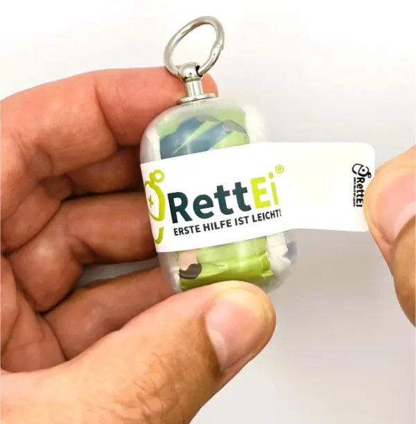 Notfall-Set-fuer-unterwegs-als-RettEi-Original-via-Erste-Hilfe-Schluesselanhaenger-mit-Beatmungstuch-zur-Mund-zu-Mund-Beatmung-mit-transparent-Kapsel-beim-oeffnen.