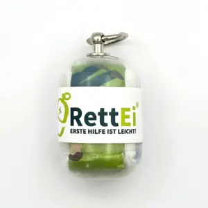 Notfall-Set-fuer-unterwegs-als-RettEi-Original-via-Erste-Hilfe-Schluesselanhaenger-mit-Beatmungstuch-zur-Mund-zu-Mund-Beatmung-mit-transparent-Kapsel-in-Seitenansicht.