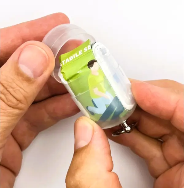 Notfall-Set-fuer-unterwegs-als-RettEi-Original-via-Erste-Hilfe-Schluesselanhaenger-mit-Beatmungstuch-zur-Mund-zu-Mund-Beatmung-mit-transparent-Kapsel-teilweise-geoeffnet.