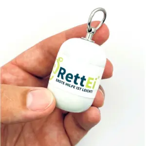 Notfall-Set-fuer-unterwegs-als-RettEi-Original-via-Erste-Hilfe-Schluesselanhaenger-mit-Beatmungstuch-zur-Mund-zu-Mund-Beatmung-mit-weiss-Kapsel-in-Hand.